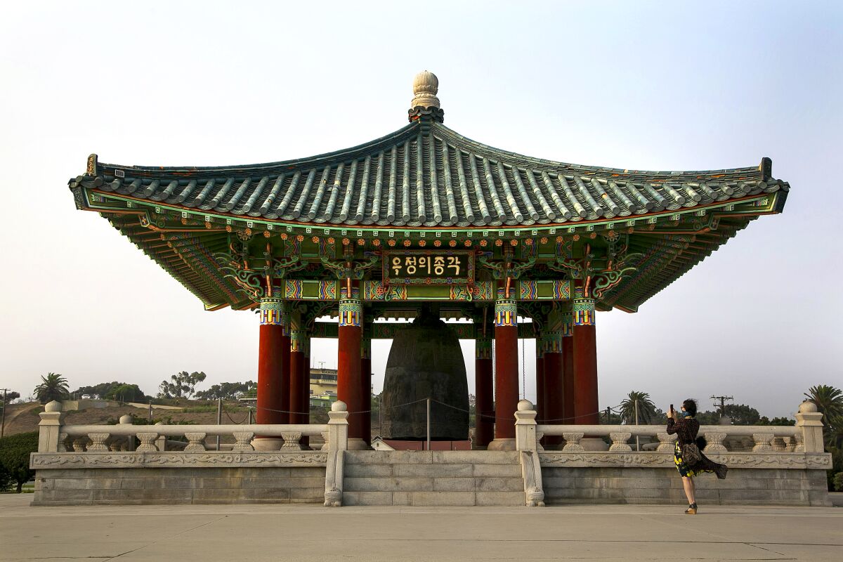 A woman photographs the Korean Bell of Friendship at Angels Gate Park