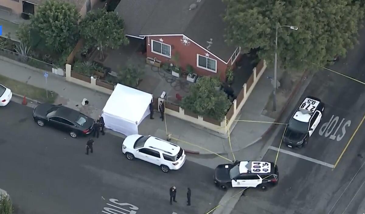 An aerial view of a white tent on a sidewalk and police cruisers parked outside a corner house.