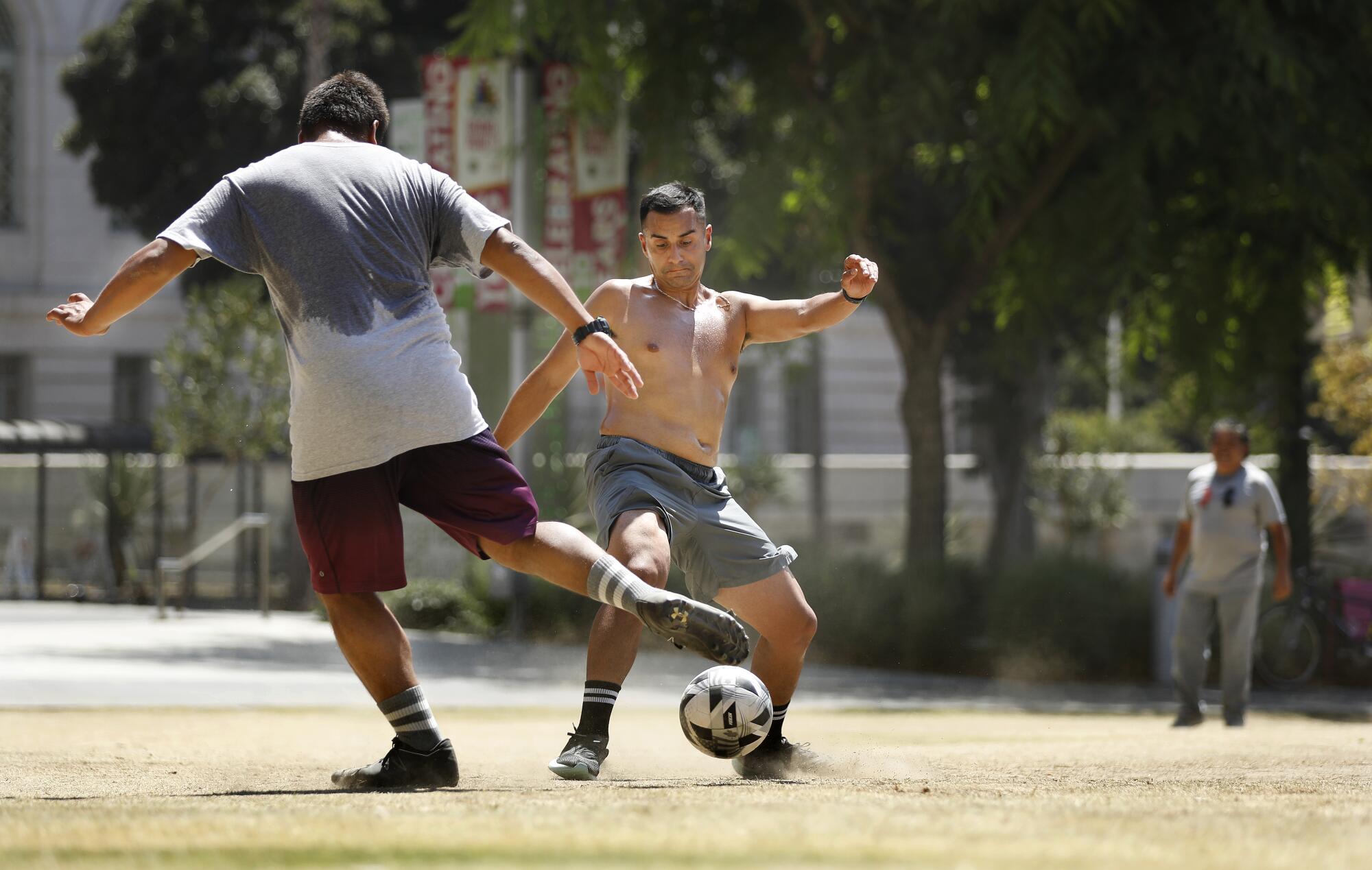 David Orantes, left, and Julio Ruiz play soccer in the hot sun at Grand Park in downtown Los Angeles