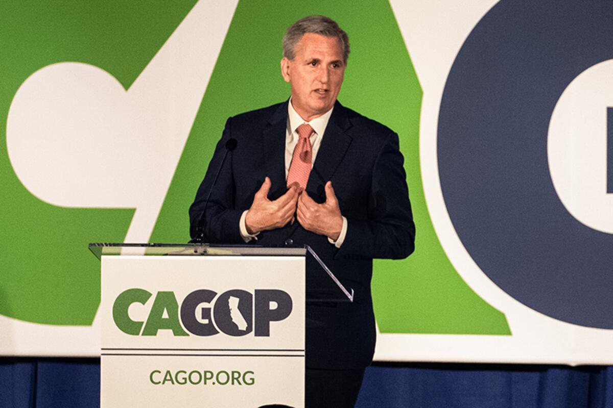 House Minority Leader Kevin McCarthy stands in front of a white, green and blue sign and gestures with his hands