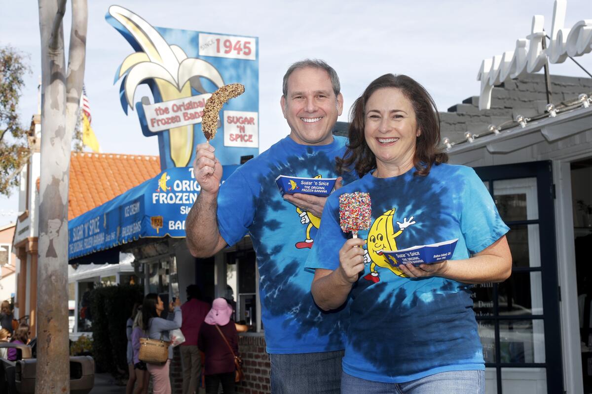 Owners Will and Courtney Alovis pose with iconic treats offered at their business, Sugar ’n Spice, which calls itself the home of the original frozen banana. The shop is celebrating 75 years on Balboa Island in Newport Beach.