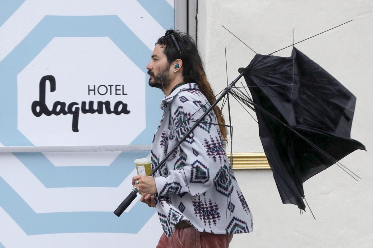 A man walks up Coast Highway past the Hotel Laguna with a tattered umbrella following a rain squall Monday morning.