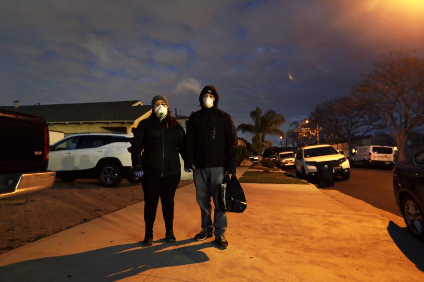 SAN PEDRO, CALIFORNIA-MARCH 31, 2020-In San Pedro, California, Mario and Ariana Mazon wear masks and gloves as they walk to their neighborhood market to get food on March 25, 20920. They try to continue their evening walks despite the restrictions brought on by the cononavirus, Covid-19. In the town of San Pedro, the coronavirus pandemic is changing the the look of daily life. (Carolyn Cole/Los Angeles Times)