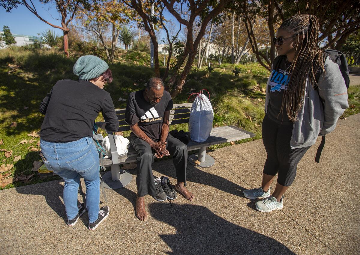 Two people speaking to a man seated on a park bench