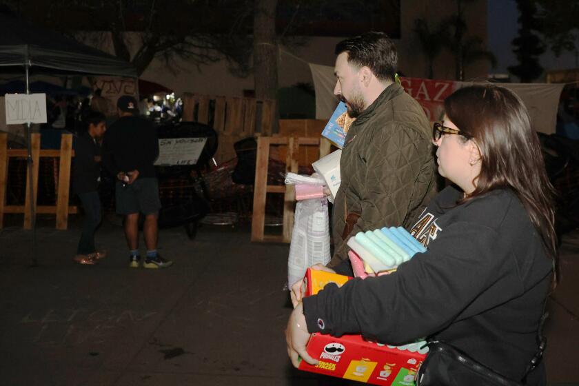 Los Angeles, CA - May 03: Sam Vasquez, left, and his girlfriend Nayellie Diaz, right, prepare to hand out supplies at the encampment at Cal State LA on Friday, May 3, 2024 in Los Angeles, CA. (Michael Blackshire / Los Angeles Times)