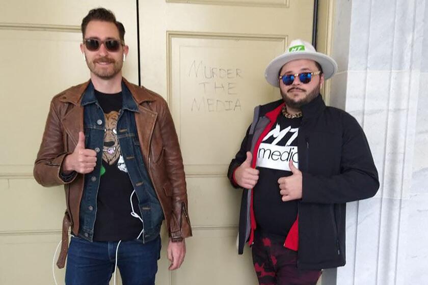 During the siege of the Capitol last Wednesday, Nick Ochs, left, and Dick NeCarlo, right, of the right-wing online streaming outlet Murder The Media pose in front of a message someone scrawled on a door. The pair insist they were covering the riot as independent reporters.
