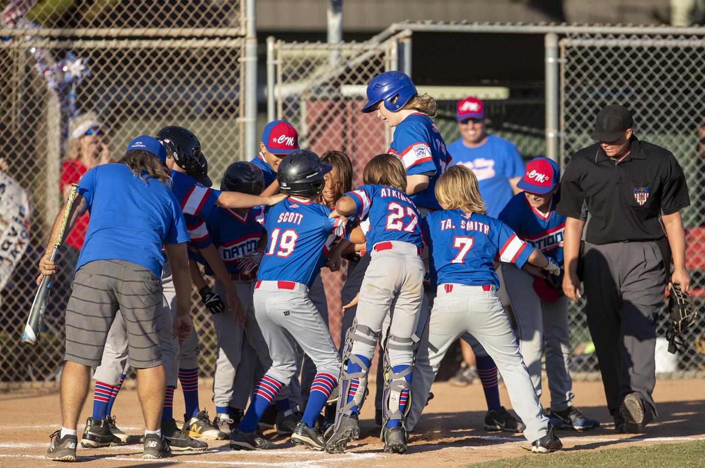 Costa Mesa National Little League's Peyton Thomas, center, is met by his teammates at the plate after he hit a solo walk-off homerun to beat Costa Mesa American Little League in the Mayor's Cup on Thursday, July 11.