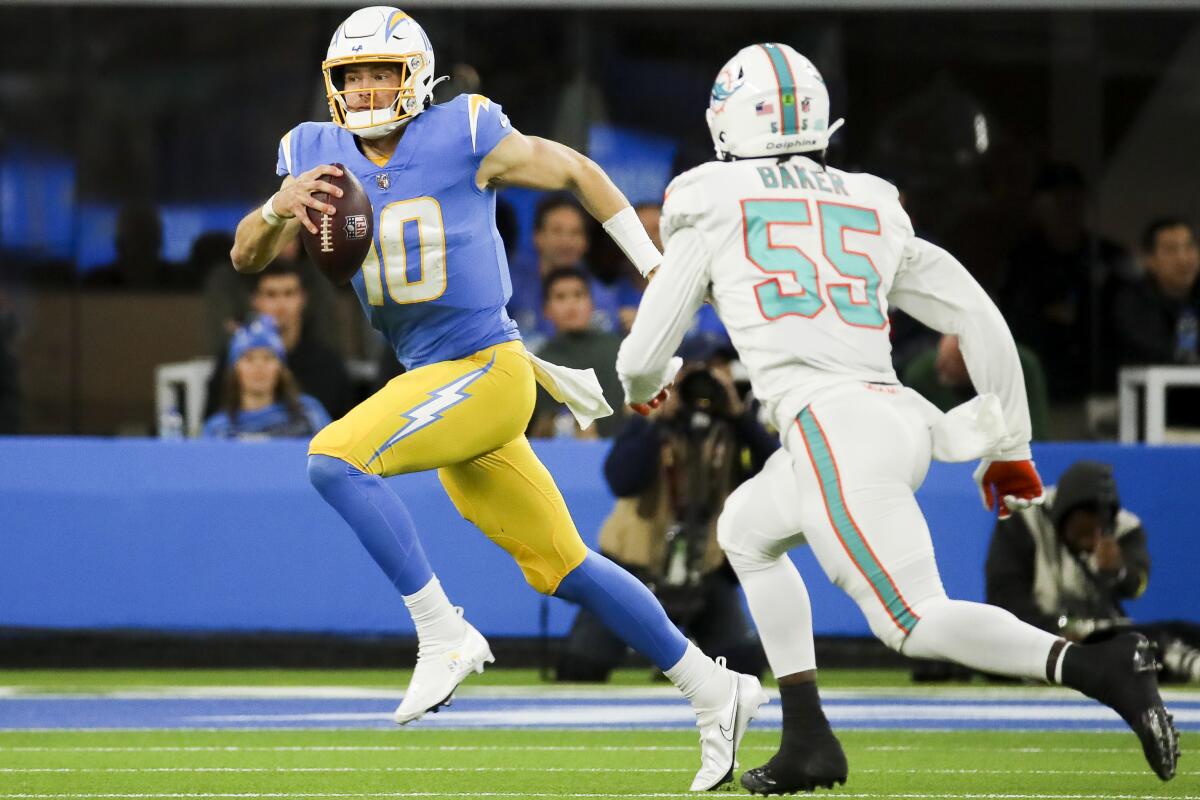 Chargers quarterback Justin Herbert, left, runs with the ball as Miami Dolphins linebacker Jerome Baker.