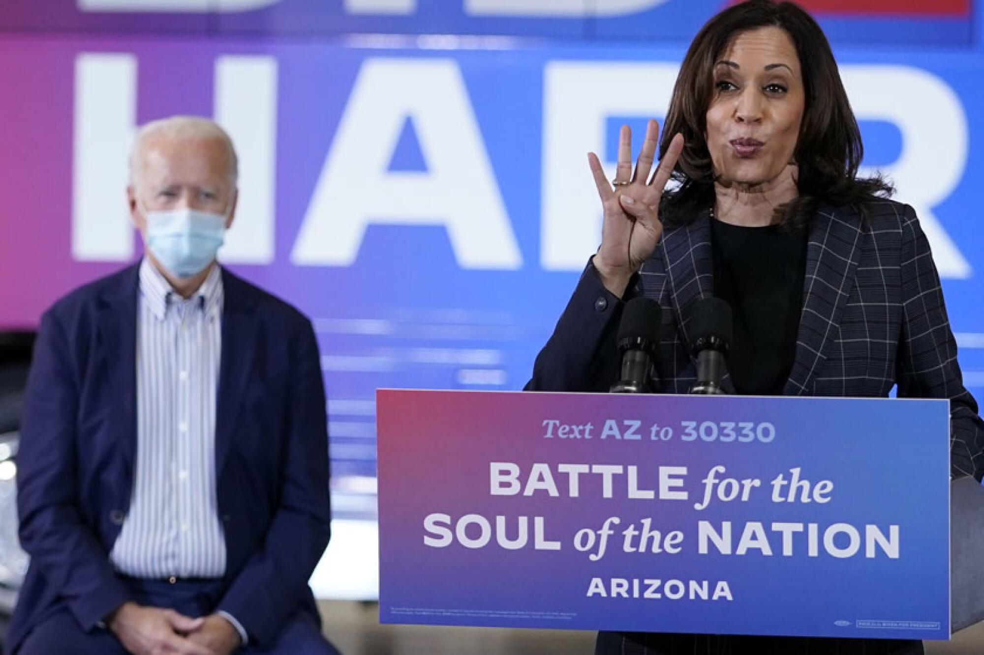 Kamala Harris speaking behind a sign that reads "Battle for the  soul of the nation: Arizona," as Joe Biden stands behind her
