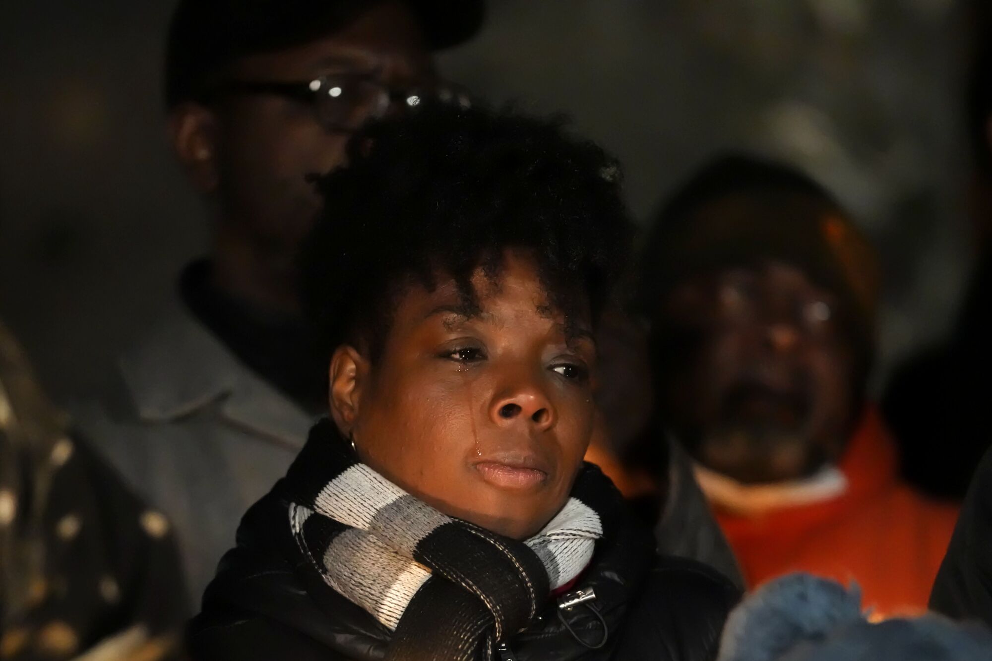 A closeup of a person with a tear-streaked face, surrounded by others outside in the dark