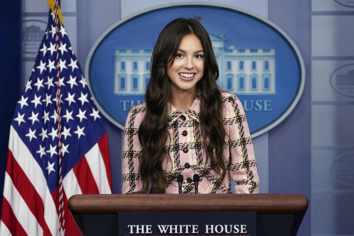 A young woman with long brown hair stands at a podium in the White House briefing room in front of an American flag