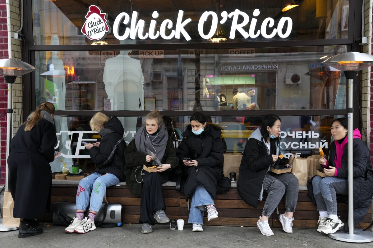 FILE - People eat their takeaway food sitting outside a cafe that is closed due to coronavirus in Moscow, Russia, Friday, Oct. 29, 2021. Russia is shortening the required isolation period for people infected with COVID-19 from 14 to seven days. The decision was announced Tuesday, Jan. 18, 2022 as Russia faces a surge of COVID-19 cases driven by the highly contagious omicron variant. (AP Photo/Alexander Zemlianichenko, File)