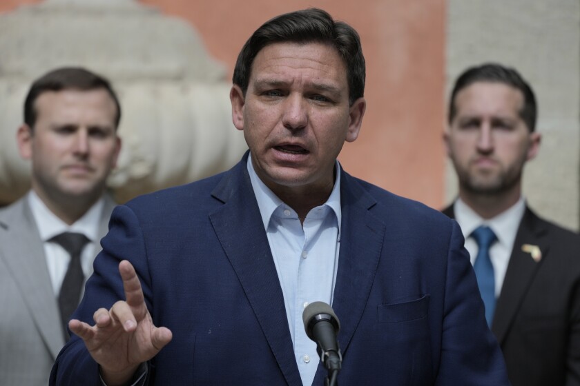 Florida Gov. Ron DeSantis standing in front of a microphone, gesturing with his right hand as he speaks.