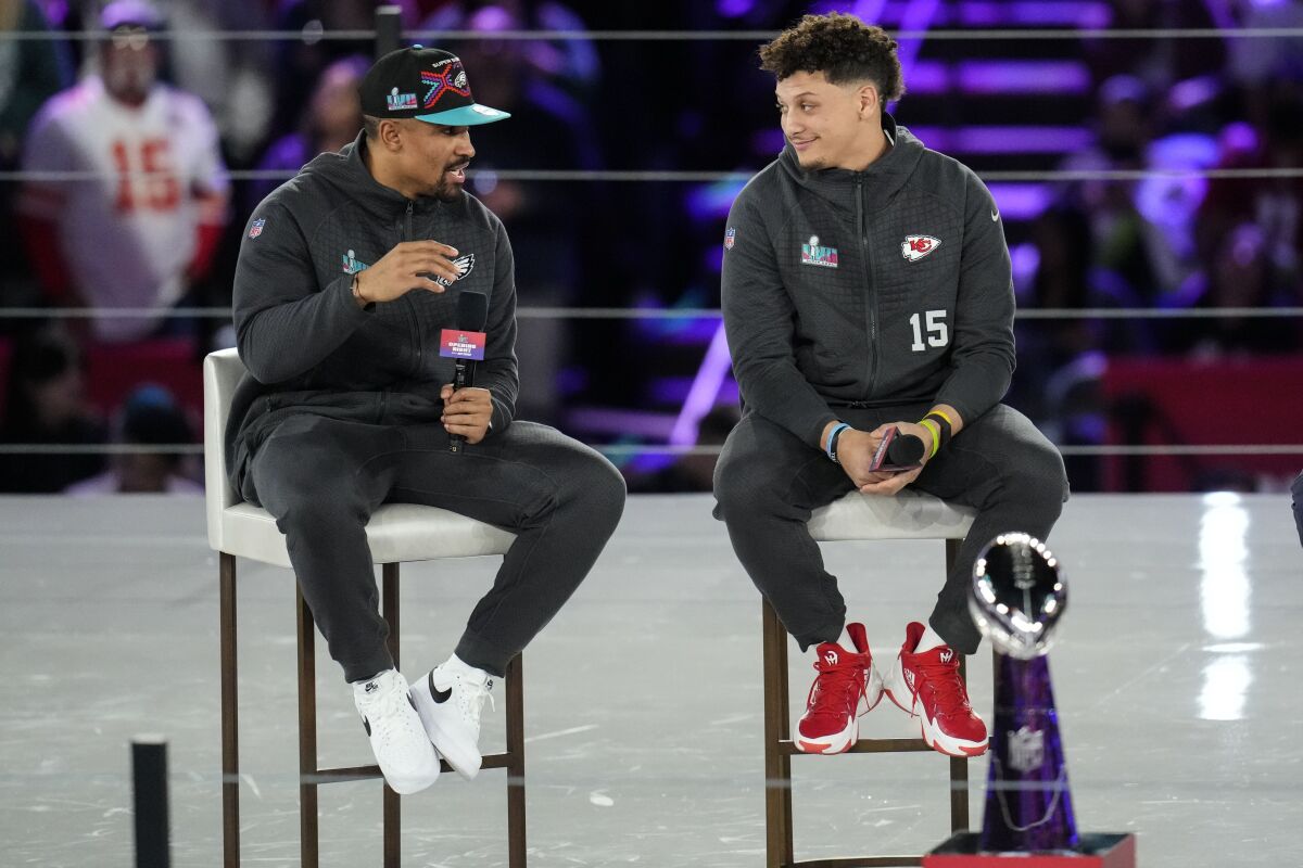 Patrick Mahomes and Jalen Hurts sit on stools onstage as they speak to reporters 
