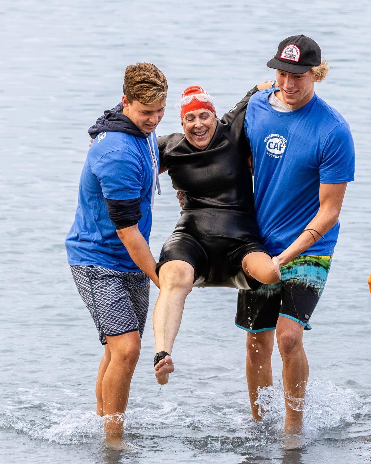 Alden Pfau and Finn Bugelli escort athlete Beth Hudson out of the water