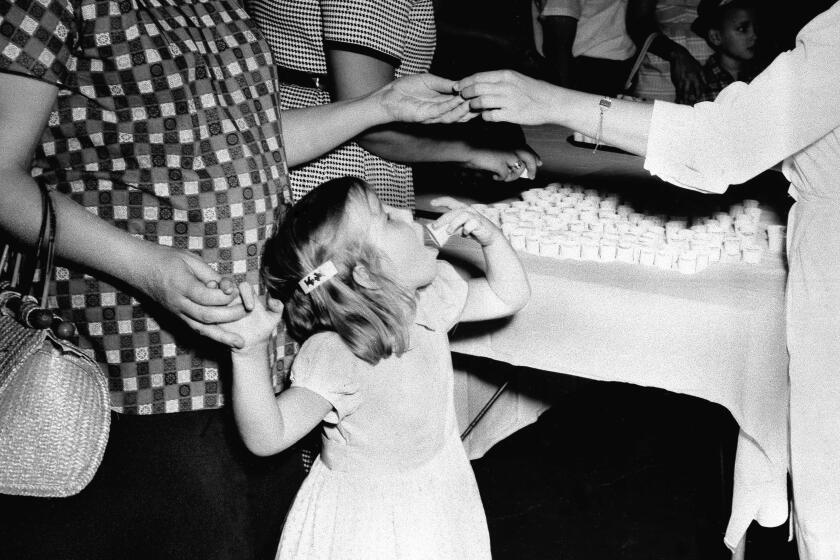 FILE - In this July 18, 1962 file photo, a girl swallows a lump of sugar coated with a dose of the Sabin polio vaccine, served in a paper cup in Atlanta, Ga. Tens of millions of today's older Americans lived through the polio epidemic, their childhood summers dominated by concern about the virus. Some parents banned their kids from public swimming pools and neighborhood playgrounds and avoided large gatherings. Some of those from the polio era are sharing their memories with today's youngsters as a lesson of hope for the battle against COVID-19. Soon after polio vaccines became widely available, U.S. cases and death tolls plummeted to hundreds a year, then dozens in the 1960s, and to U.S. eradication in 1979.(AP Photo/File)