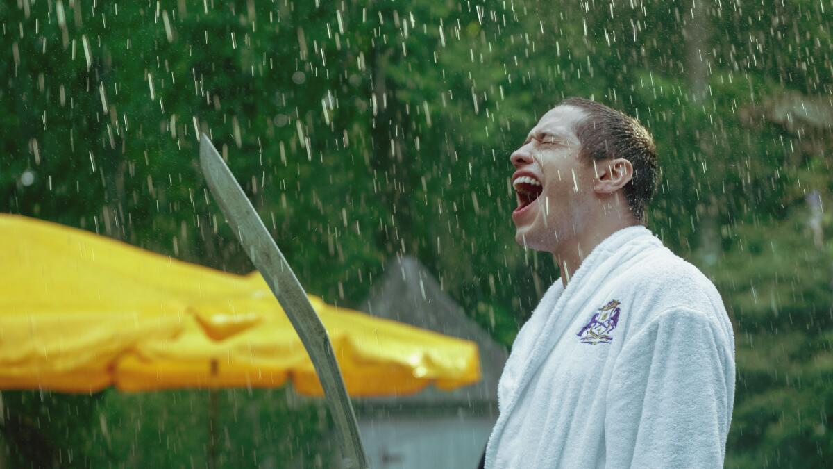 A man in a bathrobe holds a long blade in the rain.