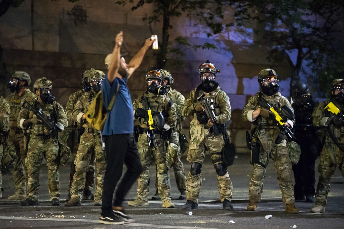 A protester holds his hands in the air while walking past a group of federal officers on July 21 in Portland, Ore.