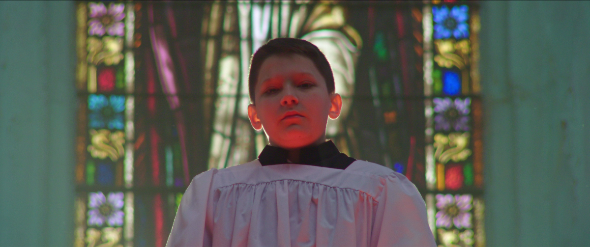 A boy dresssed as an altar boy looks into the camera in a scene from the documentary "Procession." 