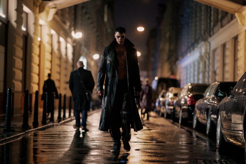 A man in a dark trench coat walks down an urban street.