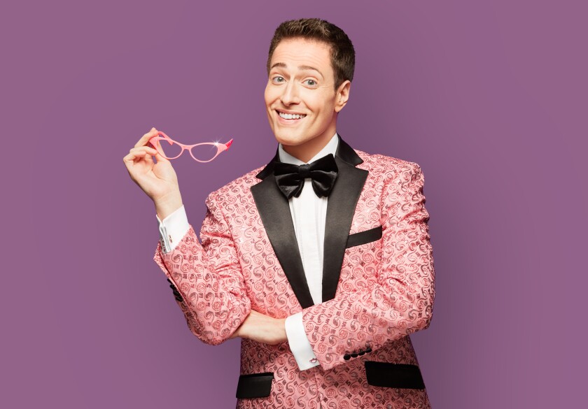 A smiling man wears a pink tux and holds pink glasses.