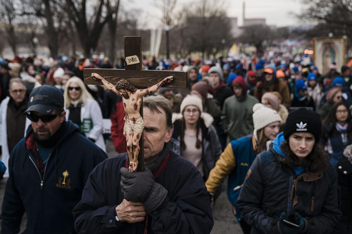 A crowd of demonstrators follows a man carrying a crucifix