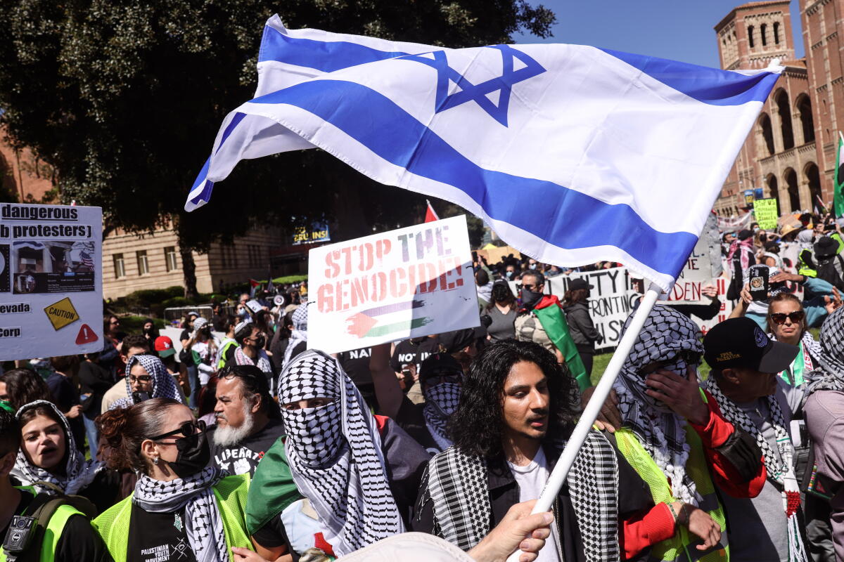 A large group of people stands holding signs and waving flags.