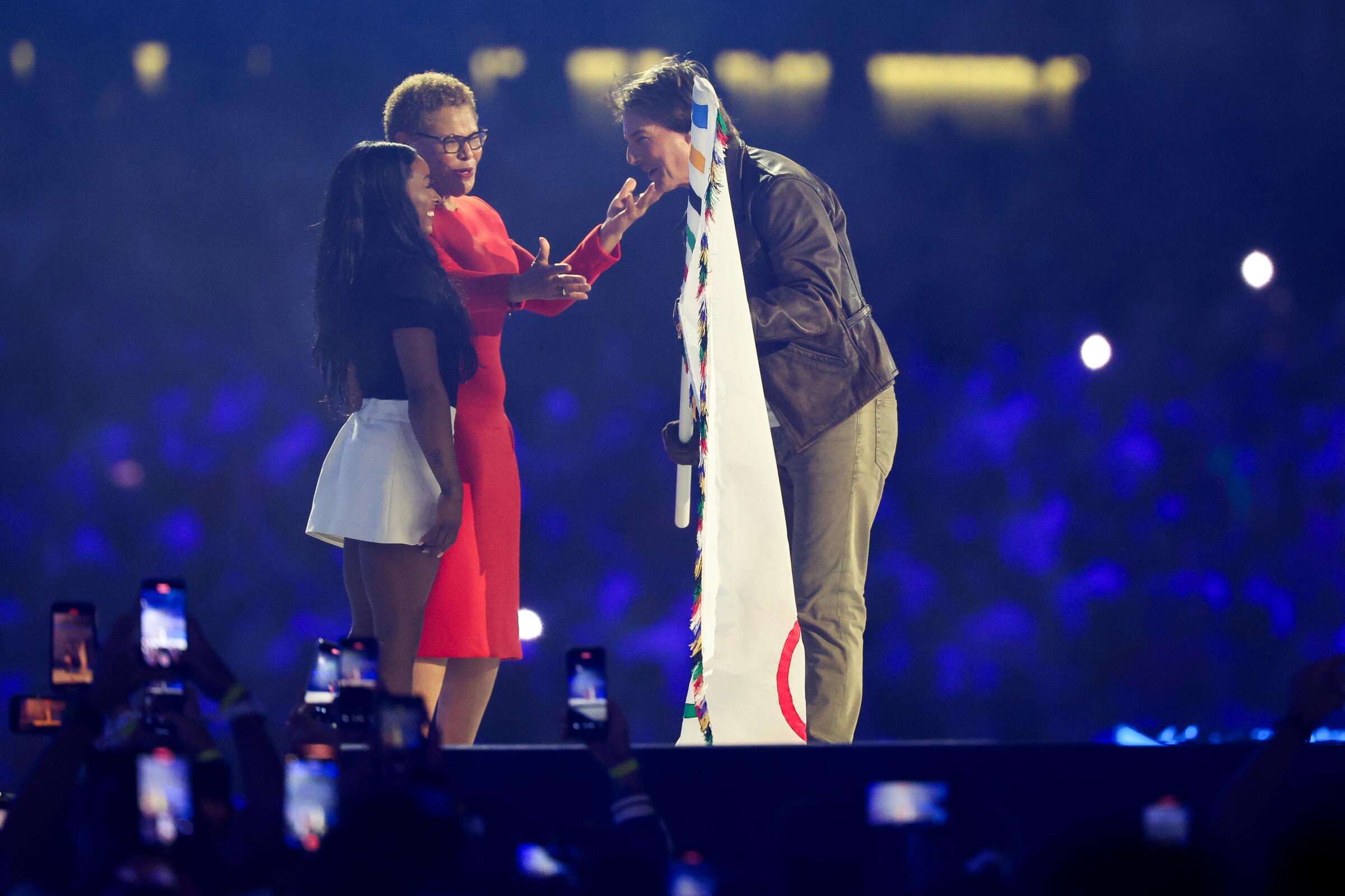 Tom Cruise holds onto the Olympic flag as he talks with L.A. Mayor Karen Bass and U.S. gymnast Simone Biles 