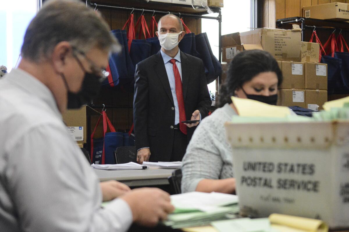 A Republican poll watcher observes an election bureau director and staffer open provisional ballots.