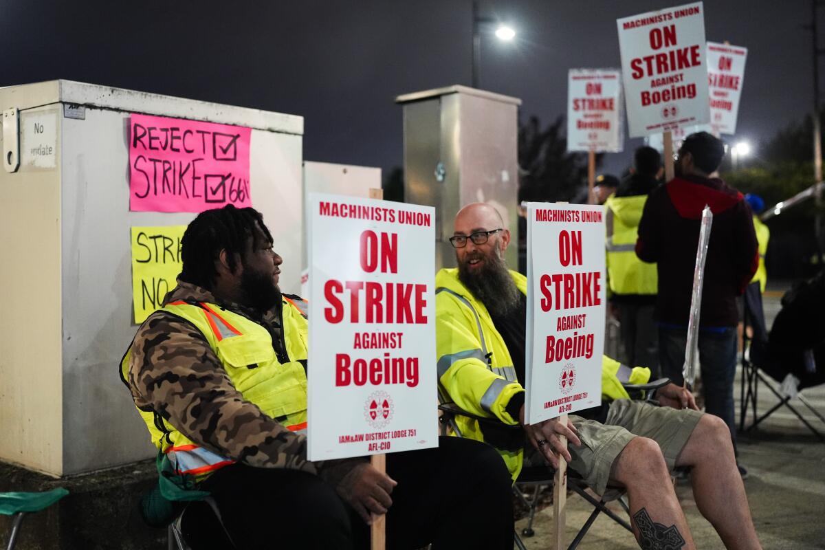 People hold boeing strike picket signs wearing yellow visibility gear