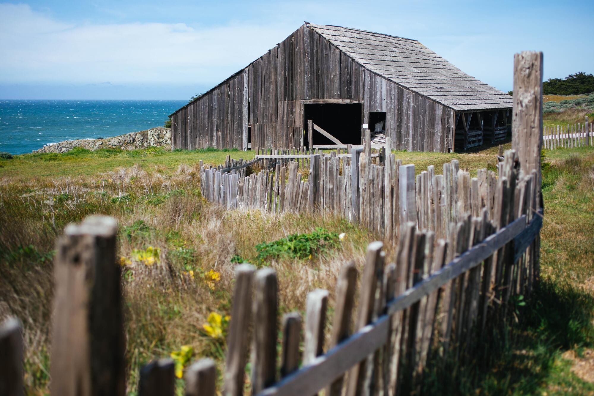 A wooden fence near a wooden barn with the ocean in the background 