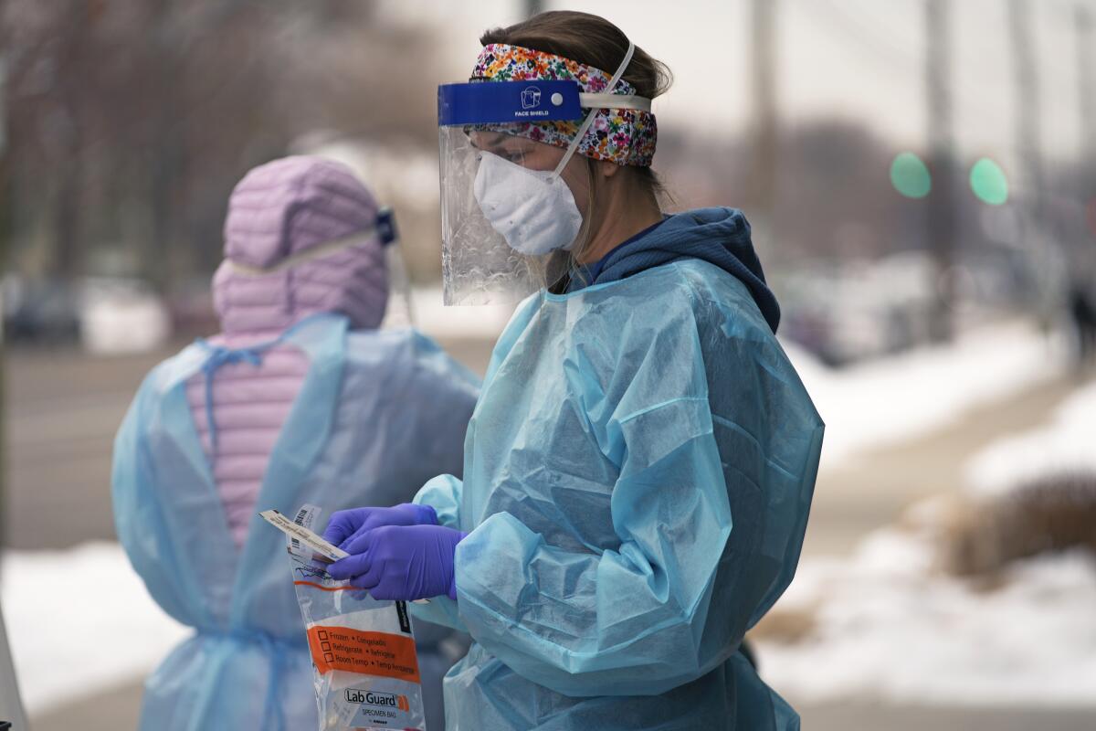 A person wearing personal protective equipment prepares a COVID-19 test outside on a snowy sidewalk.