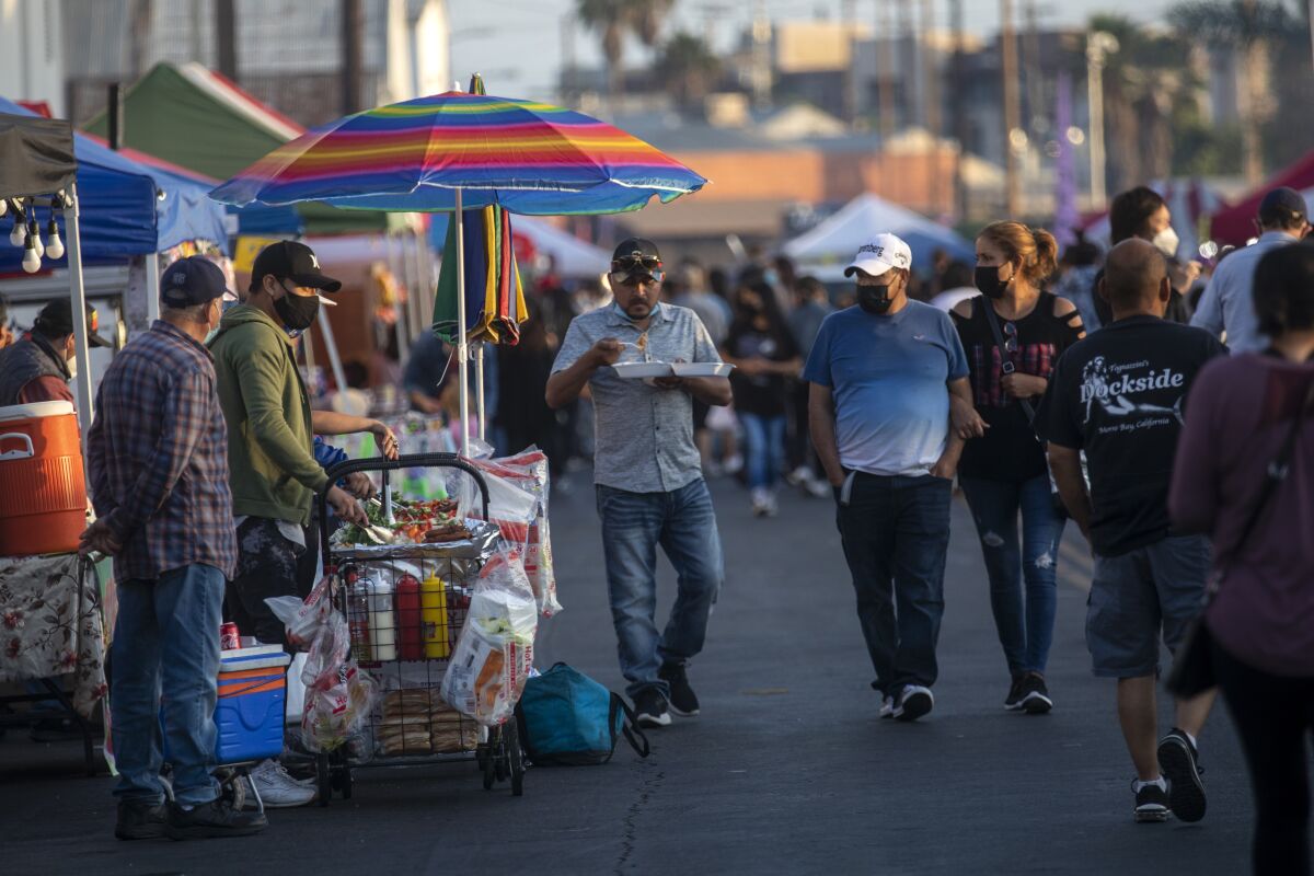 People walk past food vendors on a pedestrian street. 