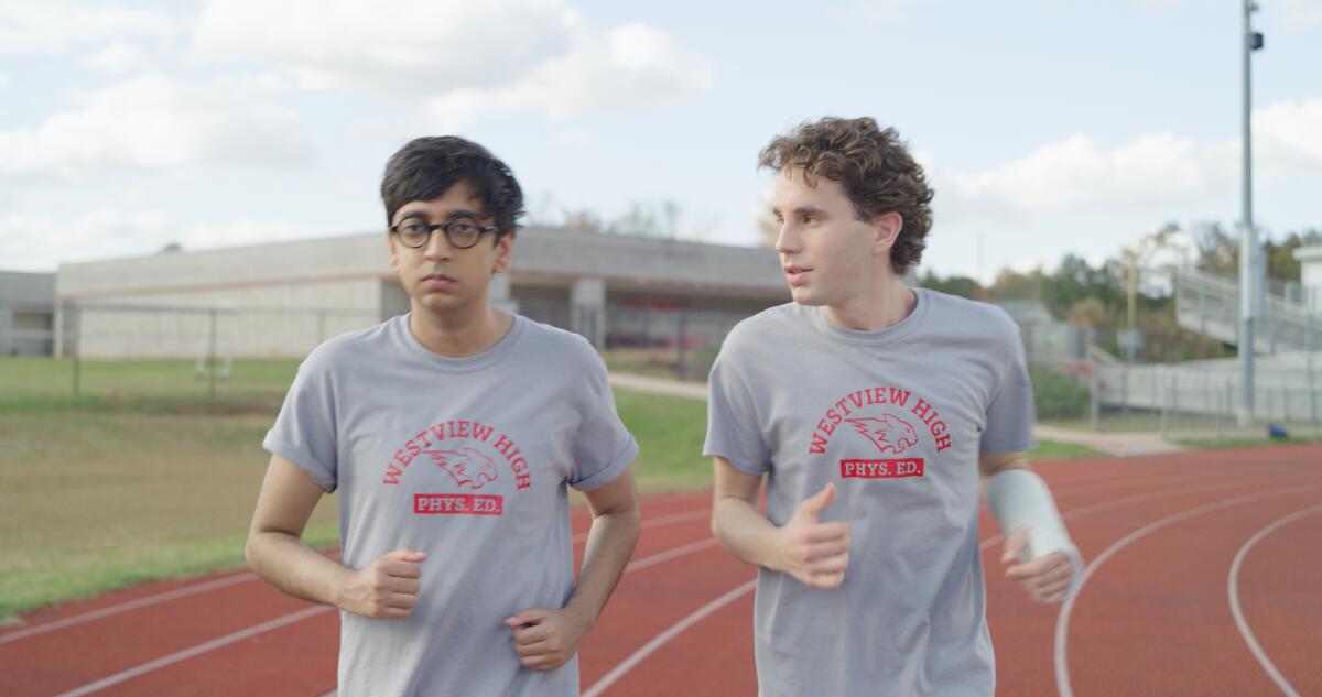 Two high school boys jog on a track.