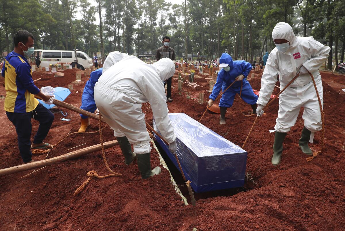 Workers in protective gear lower a coffin into a grave 