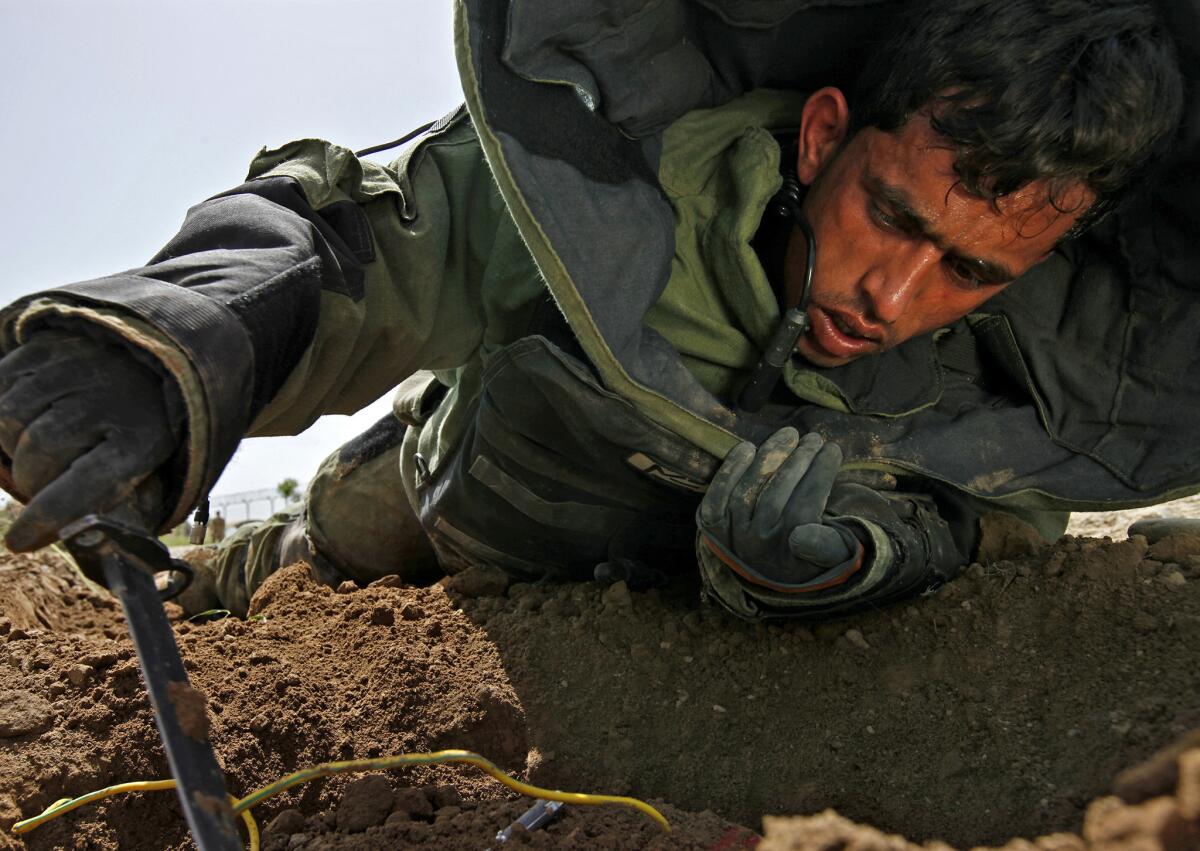 Afghan army Sgt. Huseen Bafuay wears a protective suit during a training exercise as he attempts to disable a dummy bomb buried in a road. Afghan soldiers have been known to dig at the bombs with pickaxes, but their technique has improved greatly with U.S. training and equipment.
