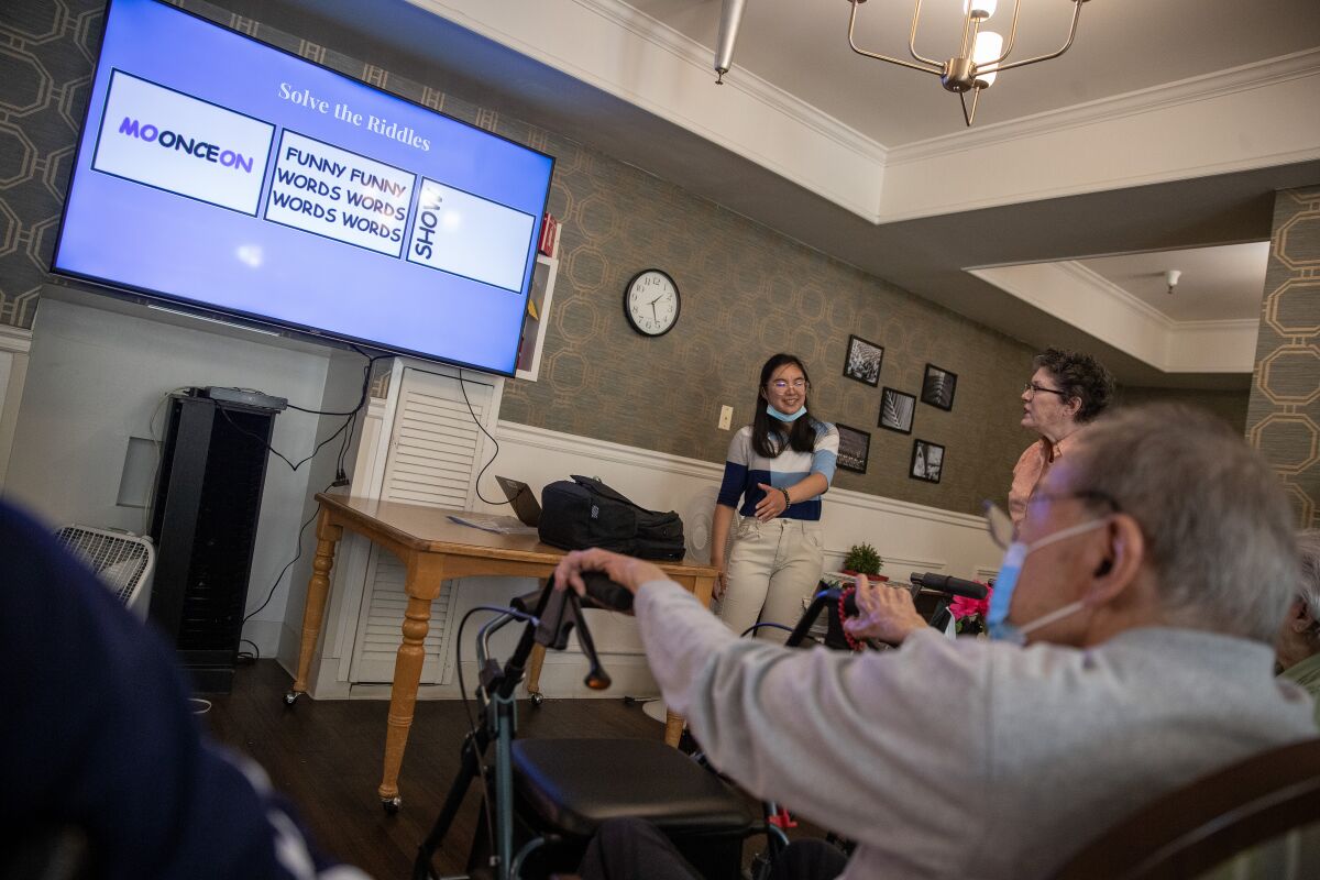 Nhi Pham stands next to a lighted screen with words on it as a seated man looks on.