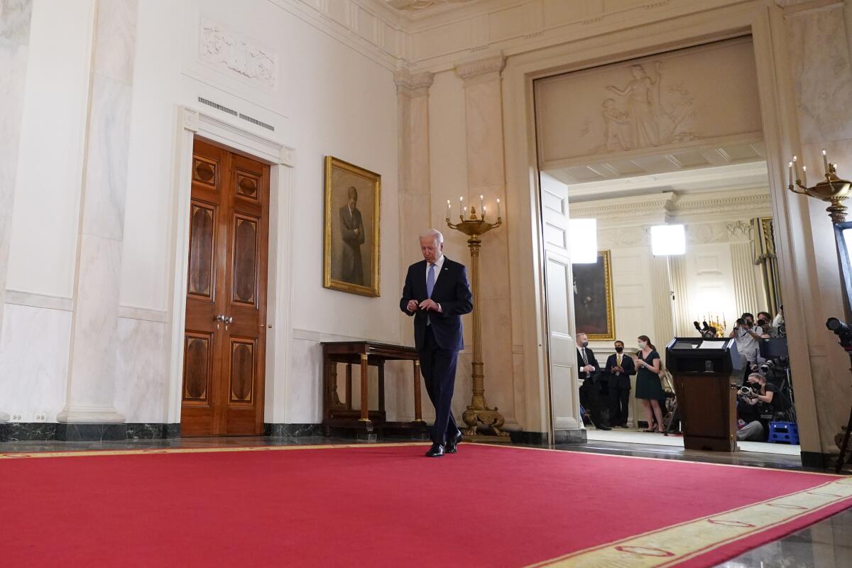 President Biden walks away from a lectern down an ornate hall 