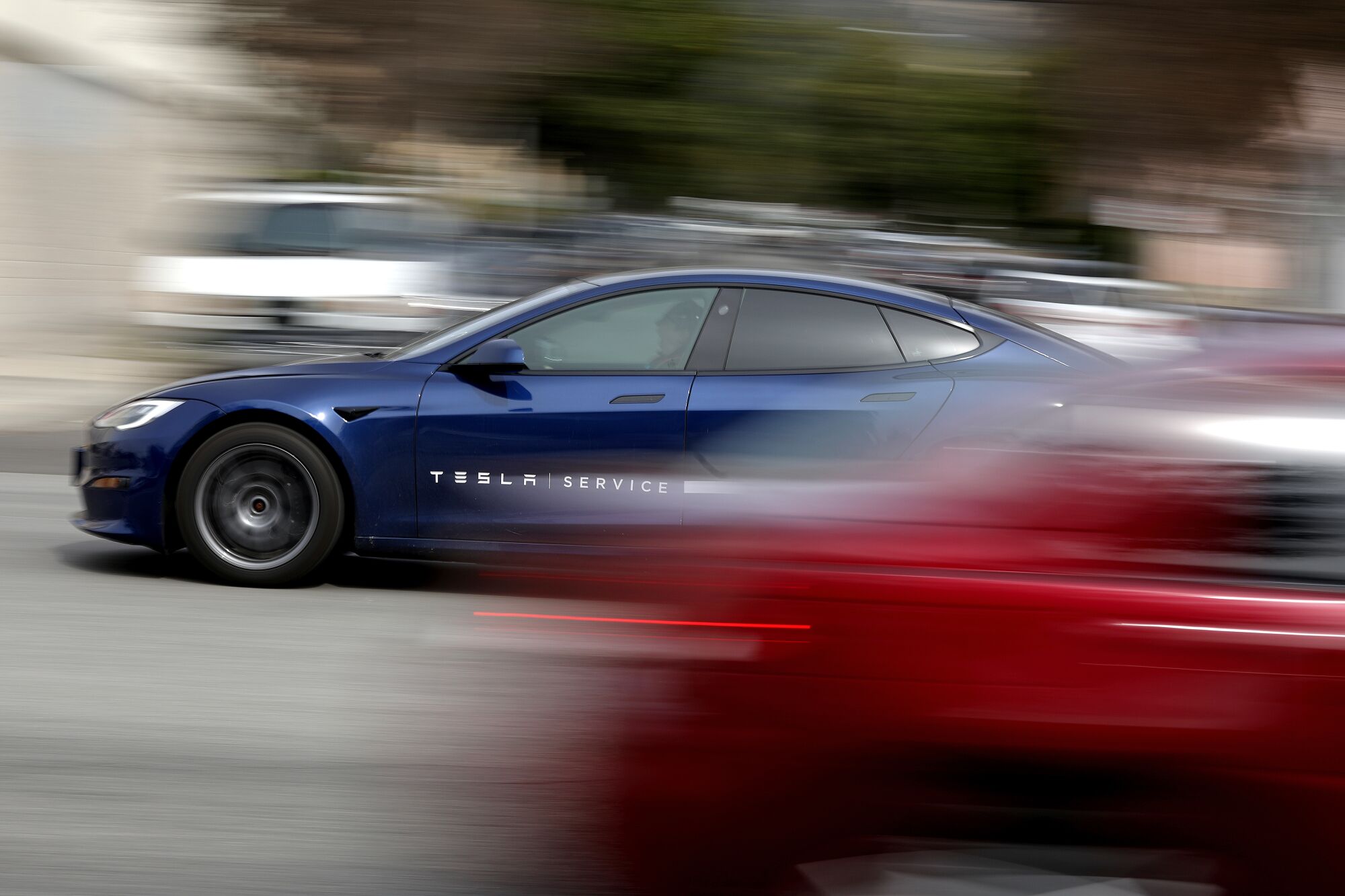 Une voiture bleue roule dans une rue, croisant une voiture rouge, qui est striée par la caméra panoramique.