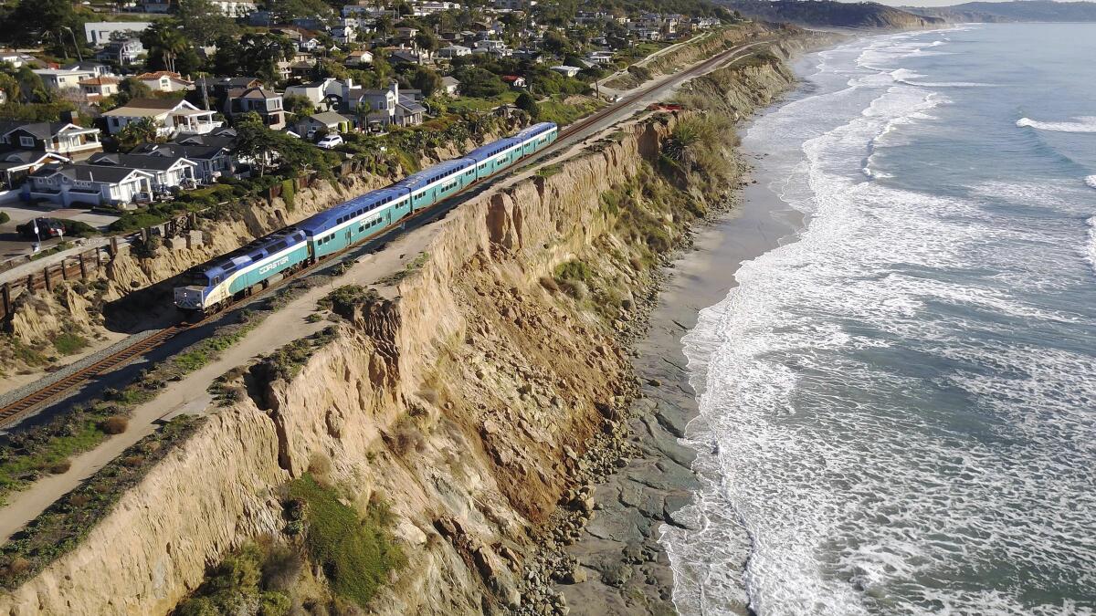A train rolls along tracks resting on a narrow ribbon of land next to seaside cliffs