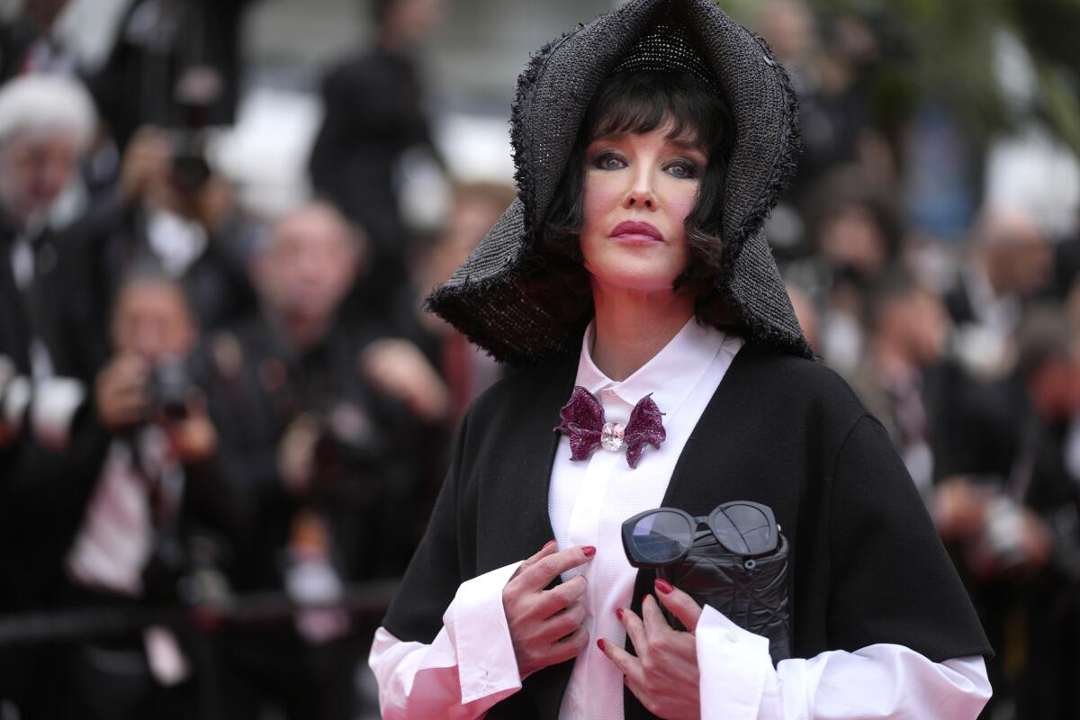 Isabelle Adjani wears a black shawl, a white long sleeved shirt with a bowtie and a gray headdress in front of photographers 