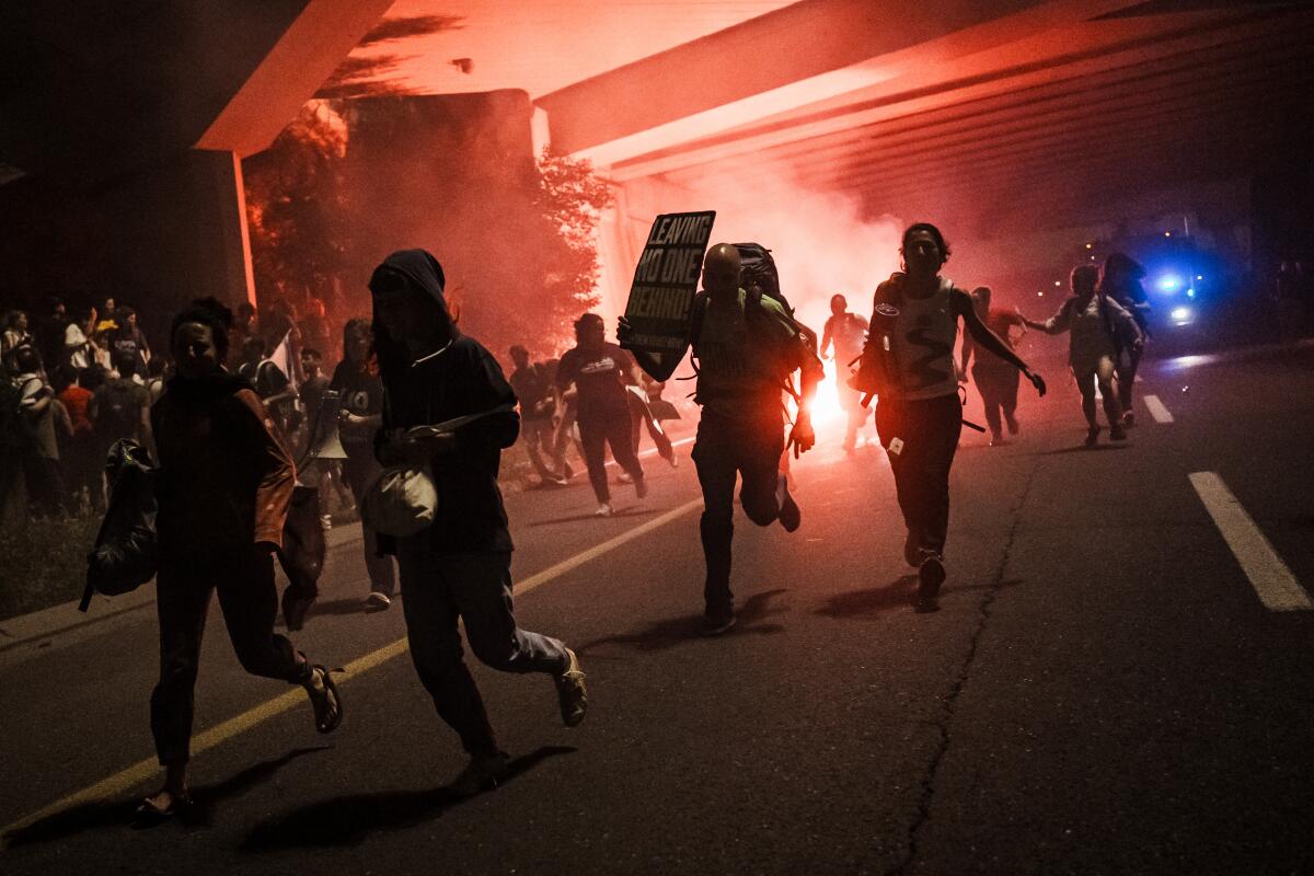 People run away as a police truck sprays skunk water onto the sit-in protest blocking a highway.