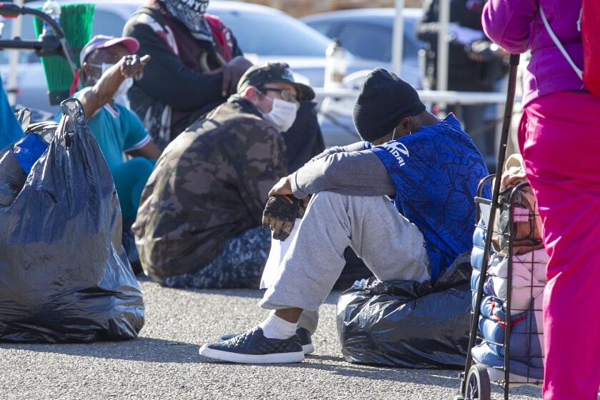 People experiencing homelessness sat in an East Village parking lot in downtown San Diego on Thursday April 14, 2020, waiting to be screened before heading to the San Diego Convention Center for temporary housing during the COVID-19 pandemic.
