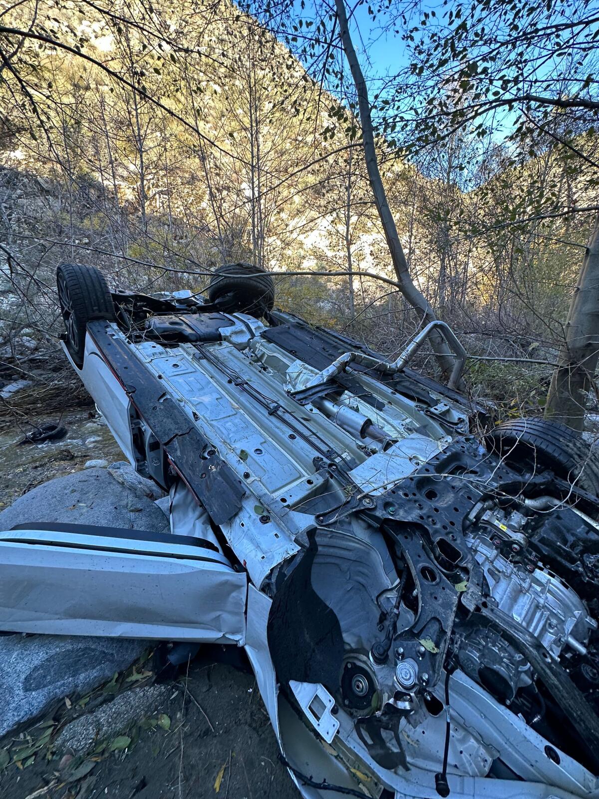A crashed car upside down amid rocks and brush