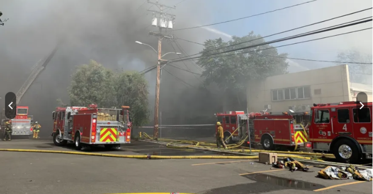 Four firetrucks sit amid thick smoke on a city street.