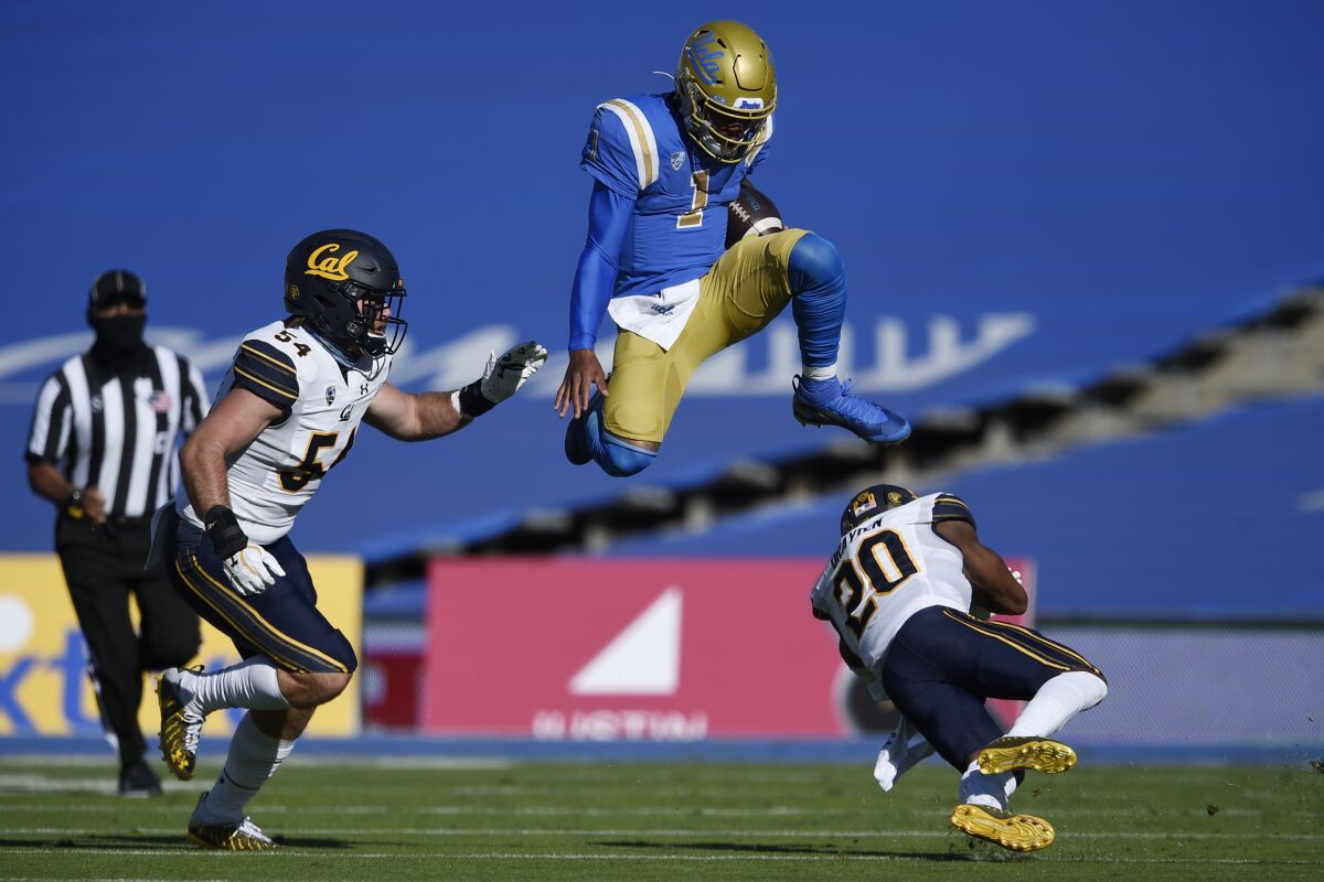 UCLA quarterback Dorian Thompson-Robinson, center, leaps over California cornerback Josh Drayden, right, on a run during the first half of an NCAA college football game as Evan Tattersall looks on in Los Angeles, Sunday, Nov. 15, 2020. (AP Photo/Kelvin Kuo)