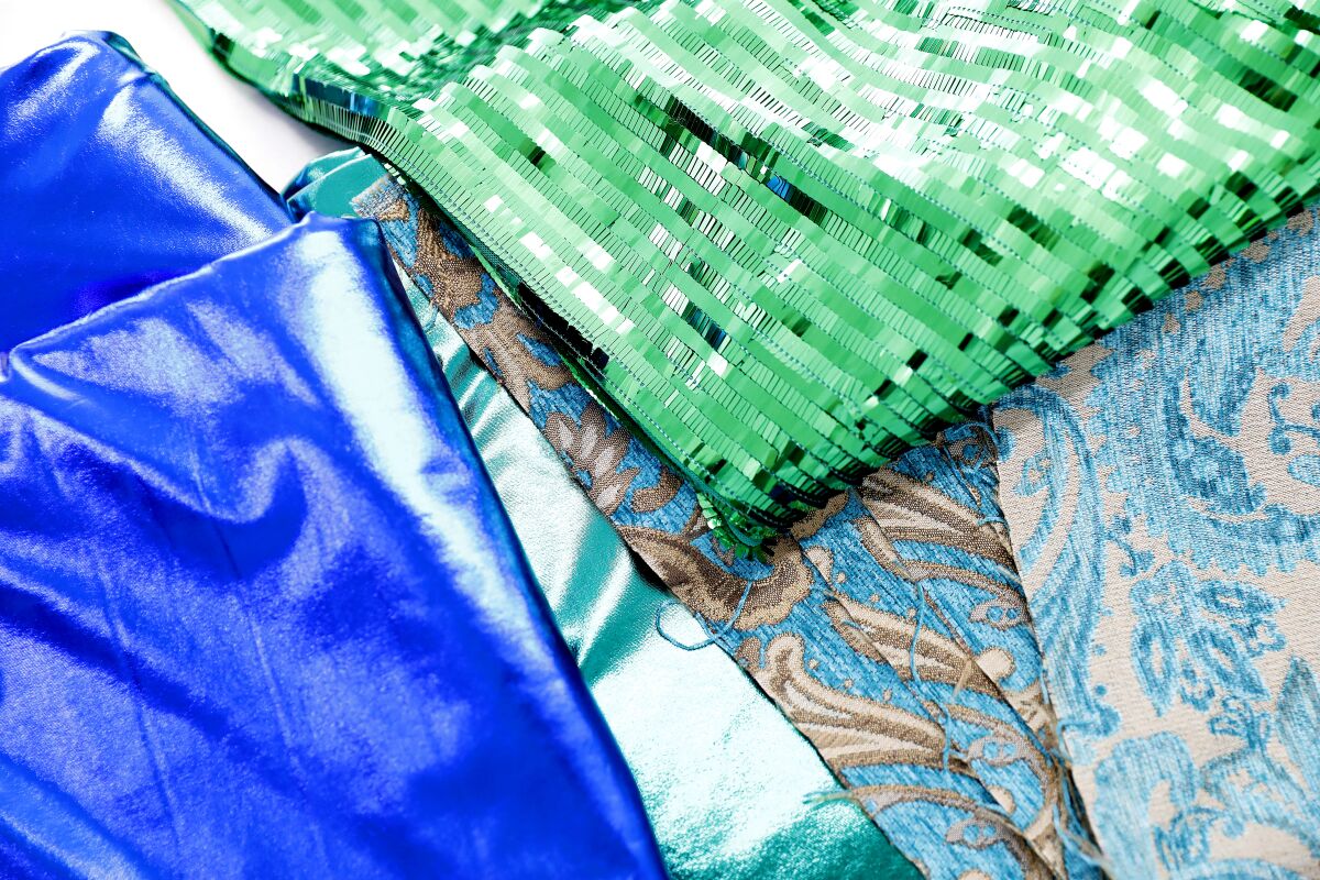 A pile of overlapping fabrics reveals swatches of green sequins, a brocade and an intense cornflower blue.