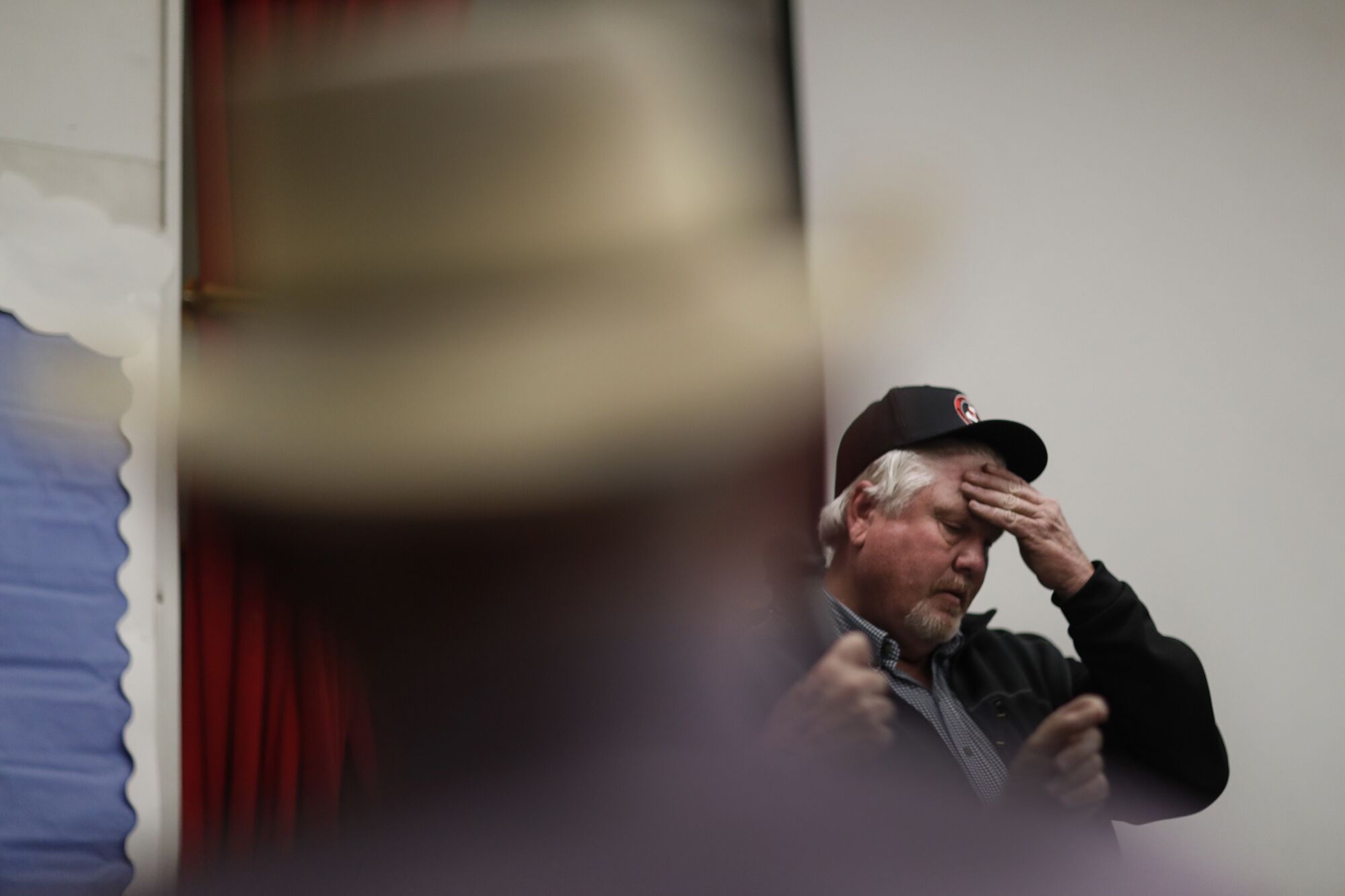 A man wearing a baseball cap puts his hand to his forehead. 