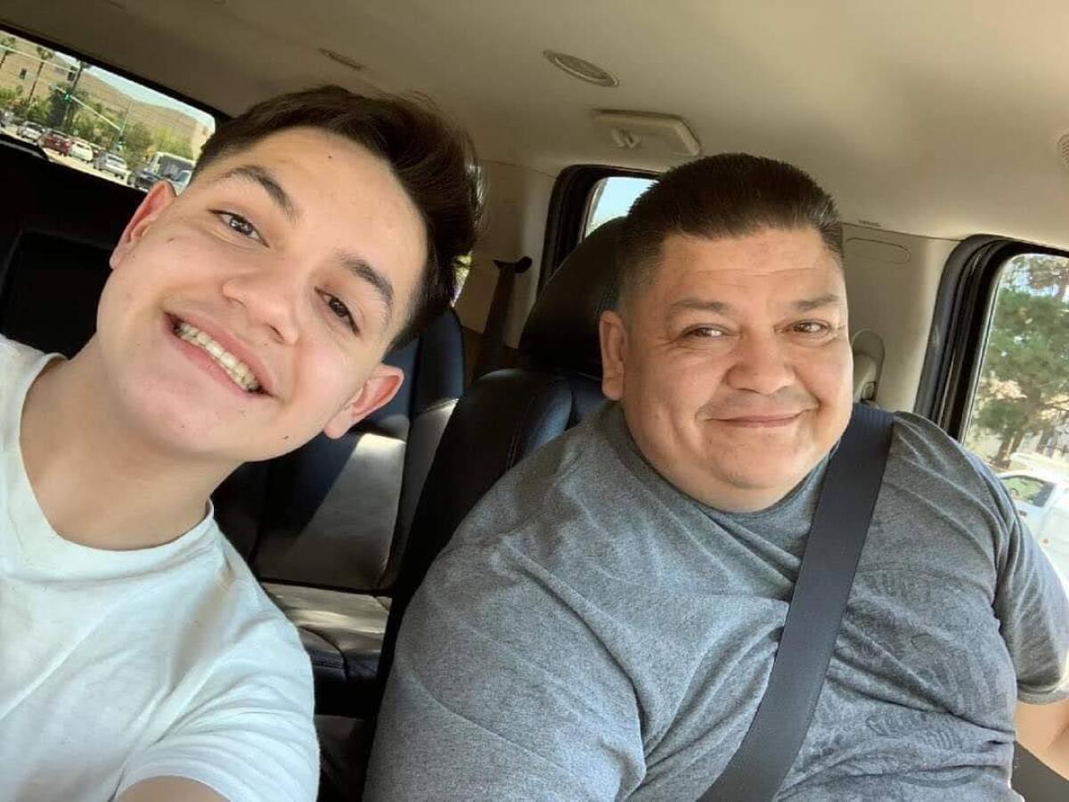 A young man and an older man smile for a photo inside a car.