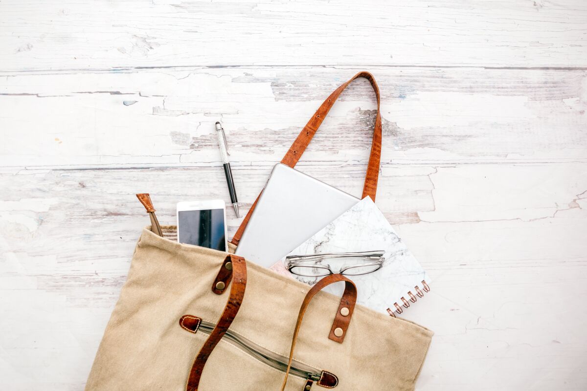 A phone, pen, paper and glasses spill out of a bag.